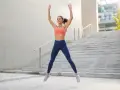 Femme en tenue de sport faisant un jumping jack devant un escalier extérieur.