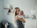 Mama tuli tulula noworodka, kołysząc go czule. W tle pokój dziecięcy z pluszakami.
