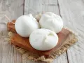 Trois boules de burrata crémeuse sur une planche en bois, parfaites pour comprendre la différence burrata et mozzarella.