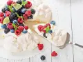 Beza Pavlova przepis: puszysta beza z bitą śmietaną i świeżymi owocami leśnymi, ozdobiona listkami mięty i plasterkami limonki.