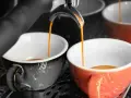 Dwie filiżanki, jedna szara, druga pomarańczowa, napełniają się aromatyczną kawą doppio.