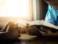 Hands clasped in prayer beside an open Bible, bathed in warm light. A moment of reflection, perhaps contemplating prayer names.