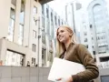 Giovane donna sorridente con laptop, cammina in una città moderna. Lavorare in Svizzera conviene, un futuro brillante ti aspetta.