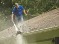 Mężczyzna myje dach myjką ciśnieniową, usuwając liście. Sprawdź mycie dachu cena i zadbaj o swój dom.