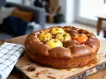 Une délicieuse flognarde aux pommes, dorée et garnie de fruits frais et de bâtons de cannelle, prête à être dégustée.