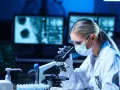 Kto pracuje w laboratorium medycznym? Młoda kobieta w okularach i masce, analizująca próbki pod mikroskopem.