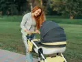 Mama z rudymi włosami uśmiecha się do wózka. Idealny przykład, jak ubrać noworodka na spacer 15 stopni.