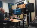 Producent muzyczny pracuje nad miksem i masteringiem w domowym studio. Na ekranie widać sekwencer, a wokół monitory studyjne.
