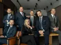 Grupa profesjonalistów w garniturach, w tym jedna kobieta, pozuje do zdjęcia.