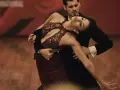 Para tańczy tango, jeden z rodzajów tańca towarzyskiego. Kobieta w bordowej sukni i mężczyzna w czarnym fraku wykonują skomplikowaną figurę.