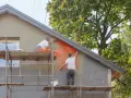 Pracownicy na rusztowaniach montują siatkę elewacyjną, przygotowując budynek do termomodernizacji.