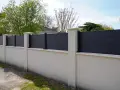 Un mur privatif moderne en composite gris, surmonté de poteaux en pierre, assure l'intimité. Distance à respecter pour une belle clôture.
