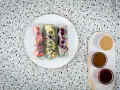 Trzy świeże spring rolls z owocami i warzywami, podane z sosami.