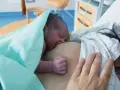 Neugeborenes Baby an der Brust der Mutter, ein Moment der stillen Geburt und des ersten Kontakts.