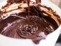 Gęsta, błyszcząca masa czekoladowa spływa z łyżki do białej miski. Idealna do fondant czekoladowy przepis.