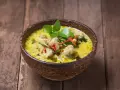 Zielone curry z kurczakiem i chili w drewnianej misce na desce.