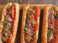 Trzy apetyczne hot dogi z frytkownicy powietrznej, z pomidorami, ogórkami, cebulą i szczypiorkiem, polane sosem.