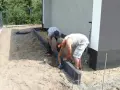 Dwóch mężczyzn układa obrzeża pod kostkę. Suchy beton pod kostkę jest przygotowywany do dalszych prac.