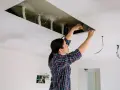 Kobieta pracuje przy suficie podwieszanym, sprawdzając rozstaw profili i instalację elektryczną.