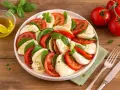 Ein klassisches Caprese Rezept: Scheiben von Tomaten, Mozzarella und frischem Basilikum, beträufelt mit Olivenöl.