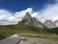 Strada tortuosa verso le Dolomiti, perfetta per una gita in moto. Montagne imponenti e cielo azzurro con nuvole bianche.