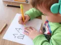 Dziecko w słuchawkach ćwiczy pisanie, wykonując ćwiczenia na dysgrafię.