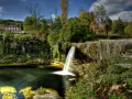 Cascadas en España: una casa rural se asoma entre la vegetación exuberante junto a una cascada que cae en un estanque de aguas verdes.