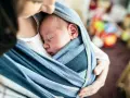 Ein Baby schläft friedlich in einem blauen Tragetuch. Der sanfte Tagesrhythmus des Babys wird durch die Nähe zur Mutter unterstützt.