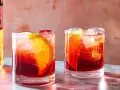 Dwa drinki Negroni z pomarańczą i lodem, obok butelki Campari. Idealny drink negroni przepis na lato.