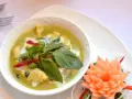 Zielone curry z kurczakiem, ozdobione bazylią i kwiatkiem z marchewki.