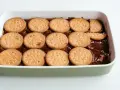 Una tarta de la abuela en preparación, con galletas redondas cubriendo una capa de chocolate en un recipiente blanco.