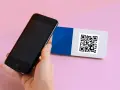 En hand håller en iPhone 6 för att scanna en QR-kod på ett kort med blått och vitt.