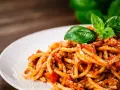 Prosty przepis na spaghetti z mięsem mielonym, podane na białym talerzu, ozdobione listkami bazylii i posypane parmezanem.
