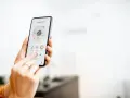 Mano usando un smartphone para encender calefacción a distancia en la sala de estar.