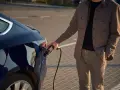 Mężczyzna podłącza ładowarkę do ciemnoniebieskiego samochodu elektrycznego. Zastanawiasz się, ile kosztuje ładowanie samochodu elektrycznego?