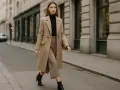 Elegancka kobieta w beżowym płaszczu i brązowych spodniach, z czarnym golfem, idzie ulicą. Czy buty w szpic są modne? Tak, te czarne botki z pewnością dodają stylu.