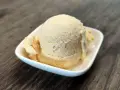 Cremiges Dulce de Leche Eis in einer weißen Schale auf Holzhintergrund.