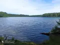 Spokojne jezioro Głęboczek otoczone lasem, z łagodnymi falami na wodzie i błękitnym niebem.