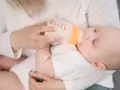 Mama karmi dziecko mlekiem modyfikowanym z butelki. Dziecko pije spokojnie, a mama czule go trzyma.