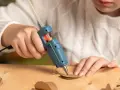 A child uses a hot glue gun to craft heart shapes from brown paper, wondering if hot glue holds up in water for their project.