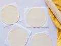 Cuatro discos de masa empanada listos para rellenar, junto a un rodillo y un paño amarillo.