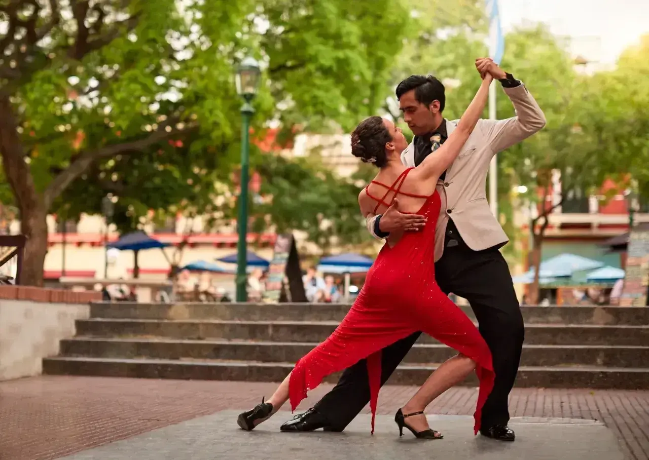 Para tańczy tango, latynoamerykański taniec towarzyski, w czerwonej sukni i eleganckim garniturze, na tle miejskiego placu.