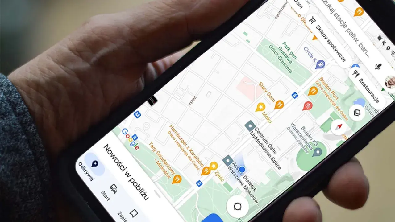 Dłoń trzyma telefon z mapą. Aplikacja do udostępniania lokalizacji pokazuje pobliskie restauracje i sklepy.