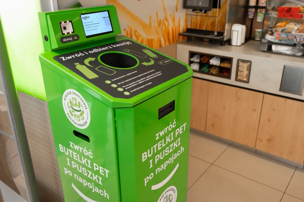 Zielony automat do zwrotu butelek PET i puszek. Skanuj kod, wrzuć opakowanie, by zdjąć zabezpieczenie sklepowe z butelki i otrzymać kaucy.