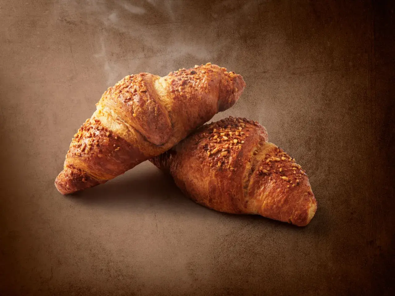 Dwa chrupiące croissanty posypane orzechami. Pyszna przekąska, ale warto pamiętać o ich kaloryczności - croissant kcal.