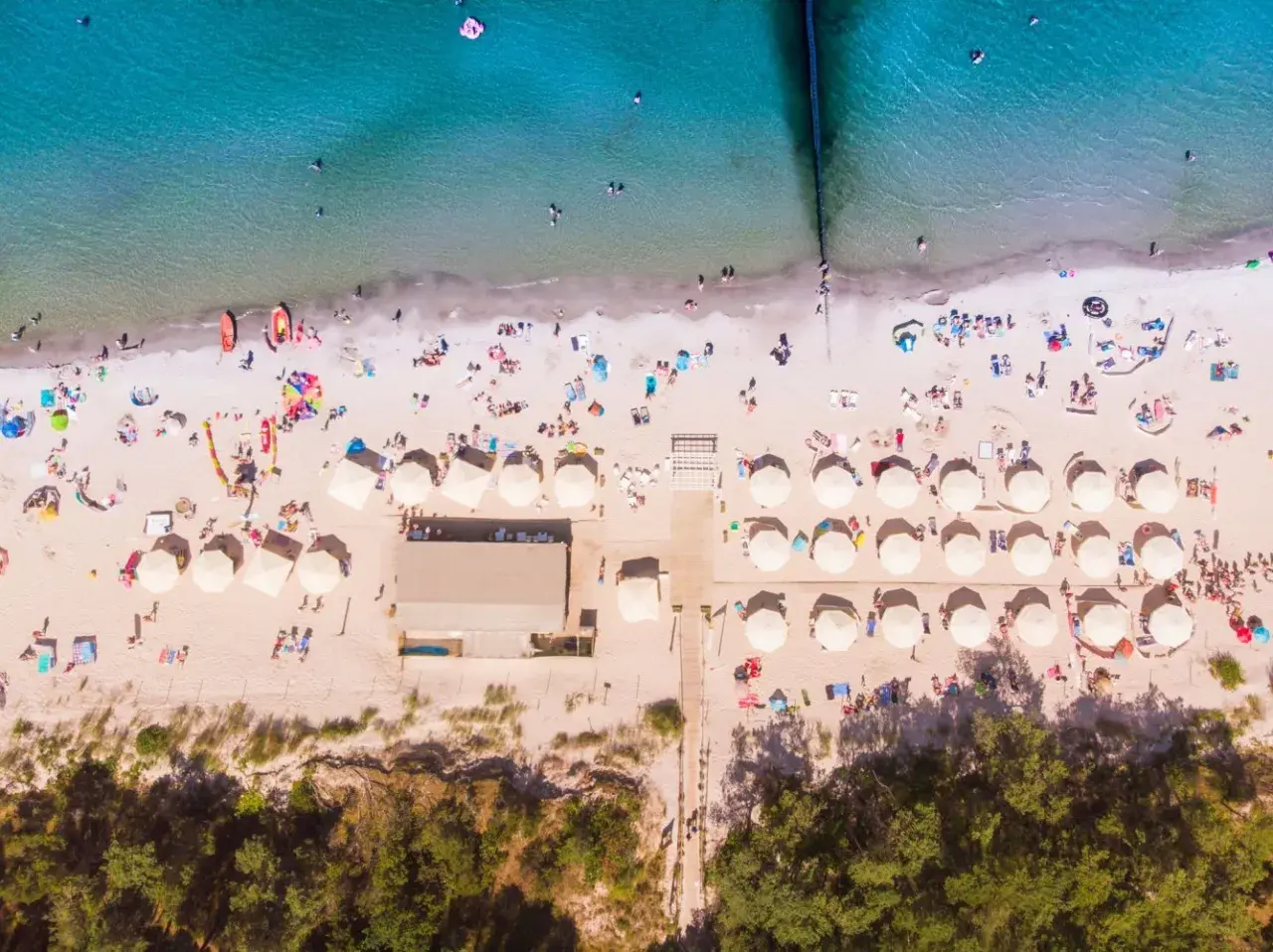 Plaża z parasolami i ludźmi, idealna na wakacje all inclusive Polska.