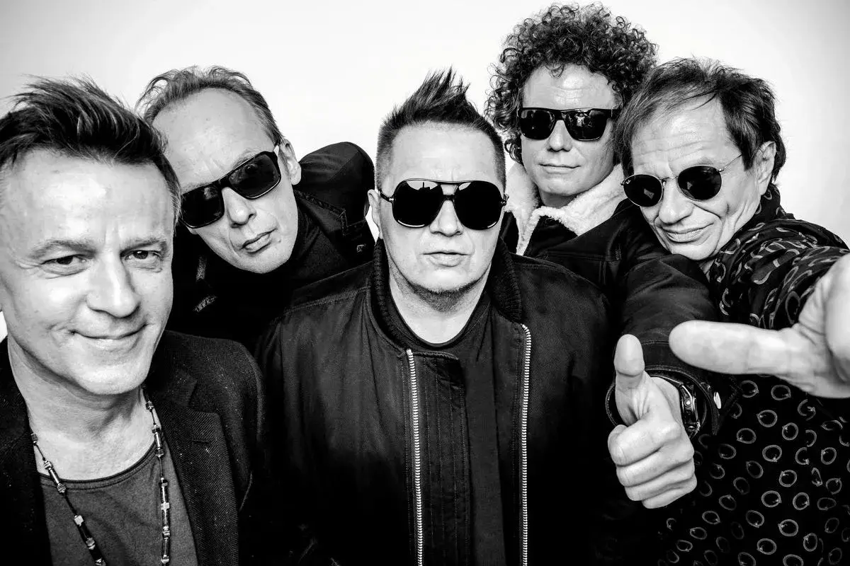 Pięciu mężczyzn w okularach przeciwsłonecznych, gotowych na koncert. Jeden z nich pokazuje kciuk w górę, jakby mówił "t.love hau! hau!".