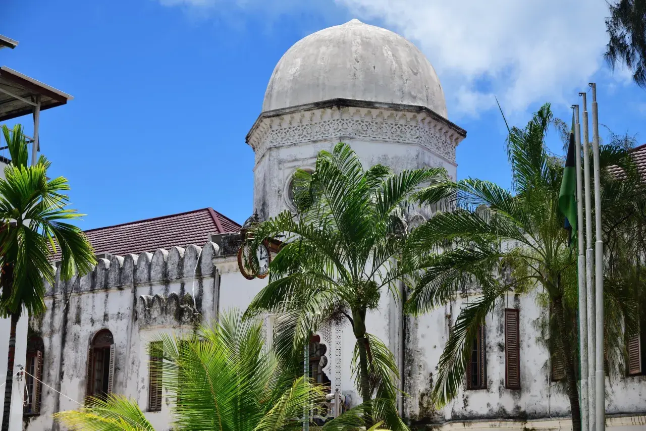 Biała, zabytkowa budowla z kopułą i palmami na tle błękitnego nieba. Klimatyczne zanzibar miasto.