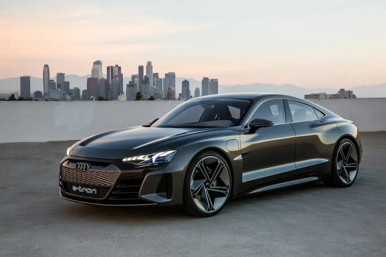 Ciemnoszary Audi e-tron GT stoi na tle panoramy miasta o zachodzie słońca.