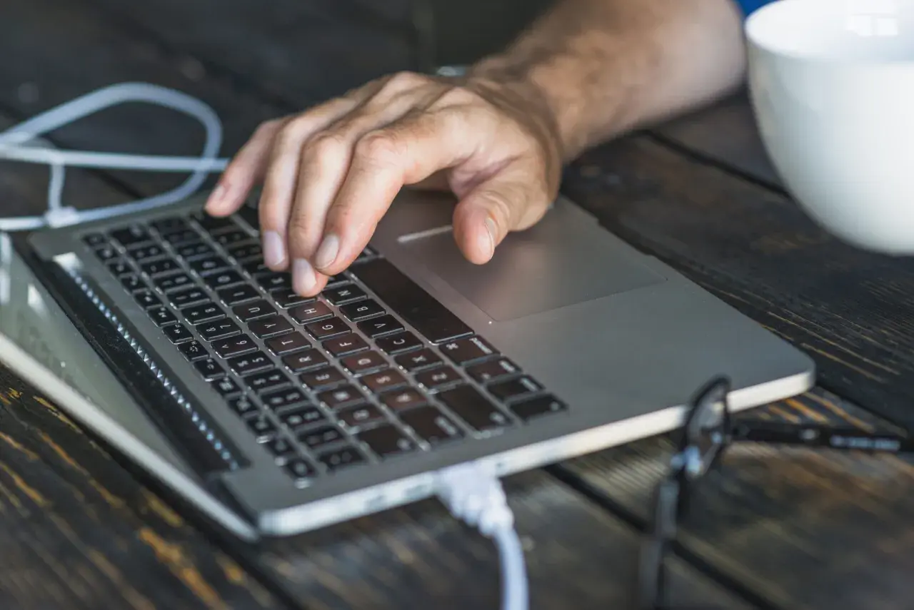 Dłoń na klawiaturze laptopa, przygotowująca się do twardego resetu. Obok biały kubek.
